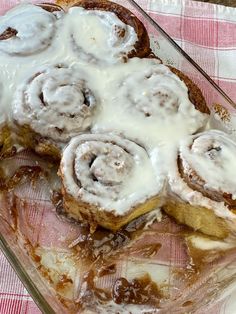 cinnamon rolls with icing in a glass dish on a pink and white checkered cloth