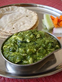 a metal plate topped with food on top of a red table cloth next to bread and vegetables