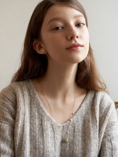 a woman with long hair wearing a white sweater and gold necklace looking off into the distance