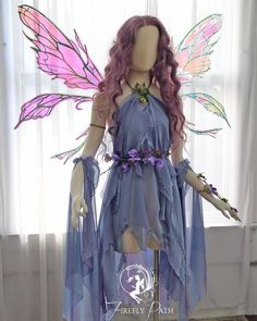 a mannequin dressed as a fairy with pink hair and purple wings is standing in front of a window