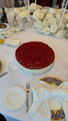 a white table topped with a cake covered in red icing next to plates and silverware