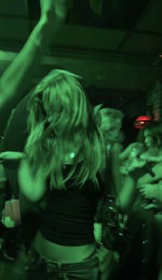 a group of people standing around each other in a room with green lights on the ceiling