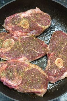 three steaks being cooked in a frying pan on the stove with seasonings