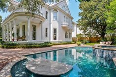 a large white house with a pool in the front yard and landscaping around it is surrounded by trees