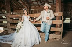 a bride and groom standing next to each other in front of a wooden fence holding hands