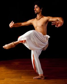 a shirtless man is doing an acrobatic pose on a wooden floor