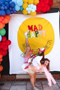 two girls are posing in front of a sign with balloons and streamers behind them