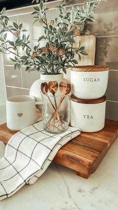 a wooden tray holding utensils and cups on top of a counter next to a potted plant