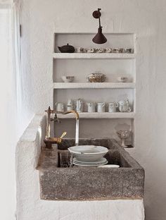 an old sink in the corner of a room with shelves above it and dishes on top