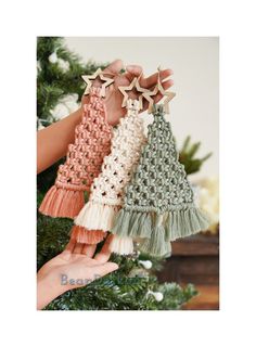 three crocheted christmas trees hanging from a tree with two hands holding them up