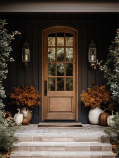 a front door with two large white vases on the steps next to it and some trees