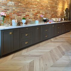 a long counter with lots of bottles and glasses on it in front of a brick wall