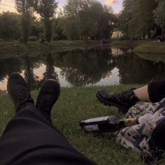 two people sitting next to each other on the grass near a lake with trees in the background