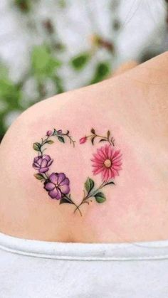 a heart shaped tattoo with flowers on the back of her shoulder and behind it is a pink flower