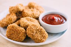 some fried food on a plate with ketchup and dipping sauce in a bowl