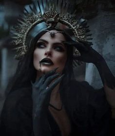 a woman with dark makeup and black gloves holding her hands up to her face while wearing a headdress