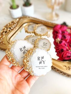 a person holding up some small white and gold brooches in front of a mirror