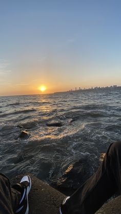 someone is sitting on the edge of a cliff looking out at the ocean