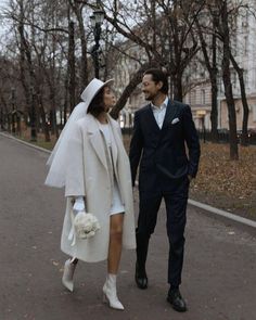 a man and woman dressed in white walking down the street with their hands behind each other