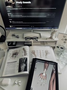 an open book sitting on top of a desk next to a computer monitor and headphones