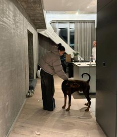 a woman standing next to a brown dog in a room with wooden floors and walls