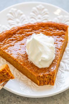 a slice of pumpkin pie on a white plate with whipped cream in the top corner