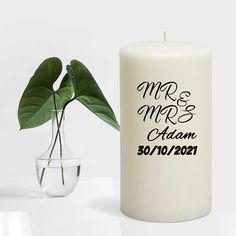 a white candle next to a vase with a plant in it and the words mr & mrs adam written on it