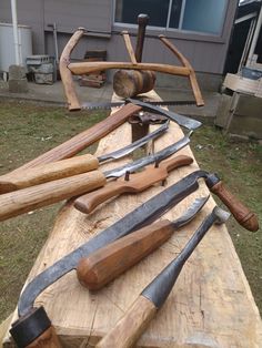 several different types of knives are on a wooden table outside in front of a house