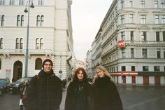 three people standing in the middle of a city street with tall buildings behind them and one person wearing a beanie