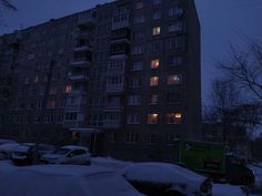 an apartment building is lit up at night in the snow with cars parked on the street