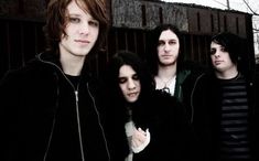 four young men standing next to each other in front of a fence with trees behind them