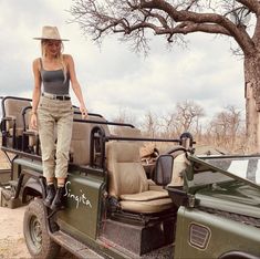 a woman standing on the back of a green jeep with safari furniture in the bed