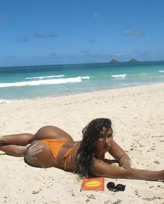 a woman laying on top of a sandy beach next to the ocean with an orange frisbee