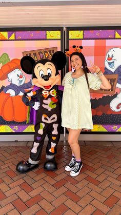 a woman standing next to mickey mouse in front of a halloween themed storefront door