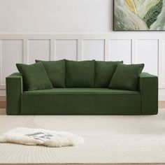 a green couch sitting on top of a white rug in a living room next to a painting