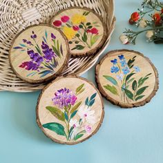 four wooden coasters with flowers painted on them sitting next to a wicker basket