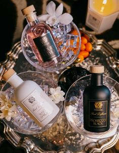 two bottles of perfume sitting next to each other on a glass tray with flowers and candles in the background