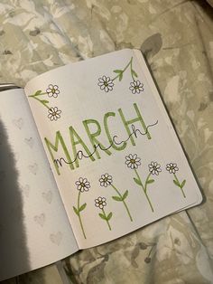 an open notebook with the word march written in green ink on it and daisies