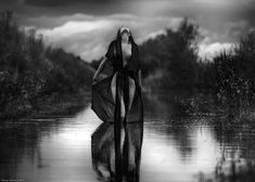 a woman is standing in the water with her back to the camera, wearing a long black dress