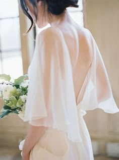 the back of a woman's dress with flowers in her hair, holding a bouquet