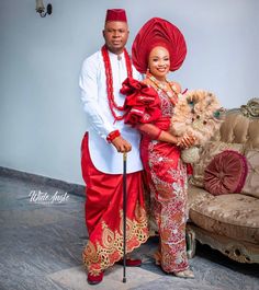 a man and woman in traditional african garb standing next to a couch with a dog