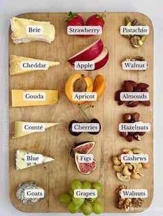 a wooden cutting board topped with lots of different types of cheeses and fruit on it