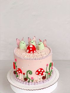 a pink cake with three little bugs on it's top and mushrooms in the middle