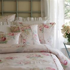 a bed with white and pink flowers on it in front of a window next to a side table