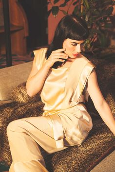 a woman sitting on top of a couch holding a cell phone to her ear and looking at the camera