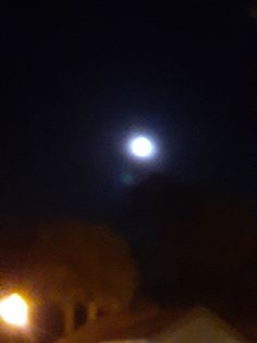 the moon shines brightly in the dark night sky over some buildings and street lights