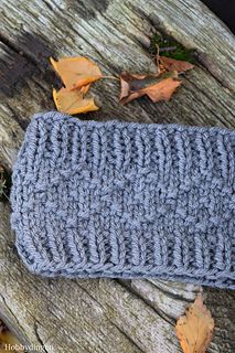 a crocheted cell phone case sitting on top of a wooden table next to leaves