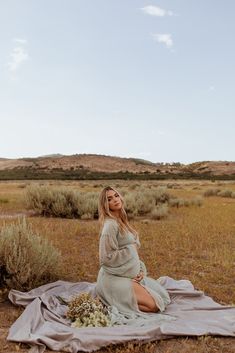 a pregnant woman sitting on a blanket in the desert