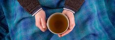 a person holding a cup of coffee on top of a blanket