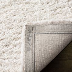 the corner of a white rug on top of a wooden floor